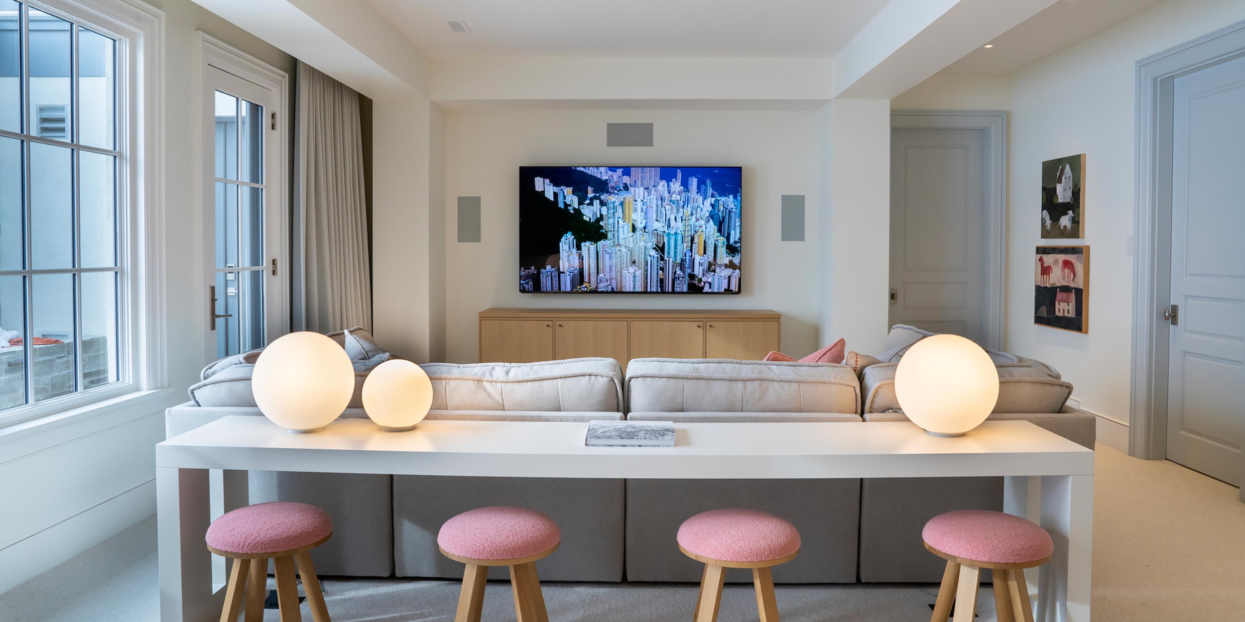 A bright and inviting media room with a wall-mounted TV, soft neutral furniture, and elegant decor, offering a cozy entertainment space.