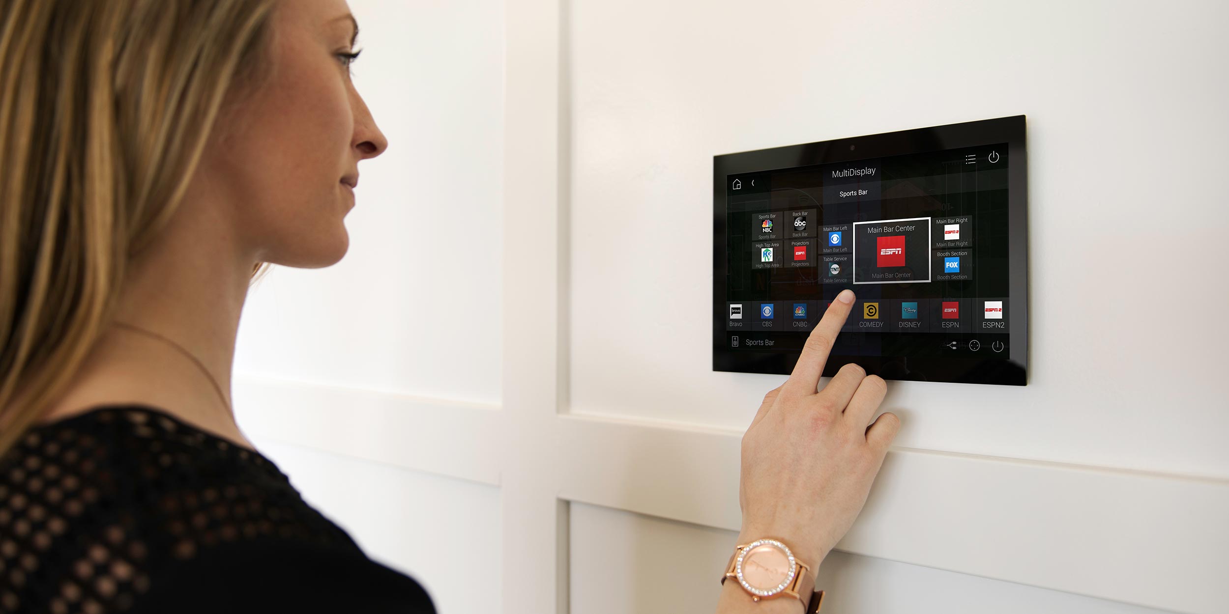 A woman interacting with a sleek, wall-mounted smart home control panel displaying various automation options.